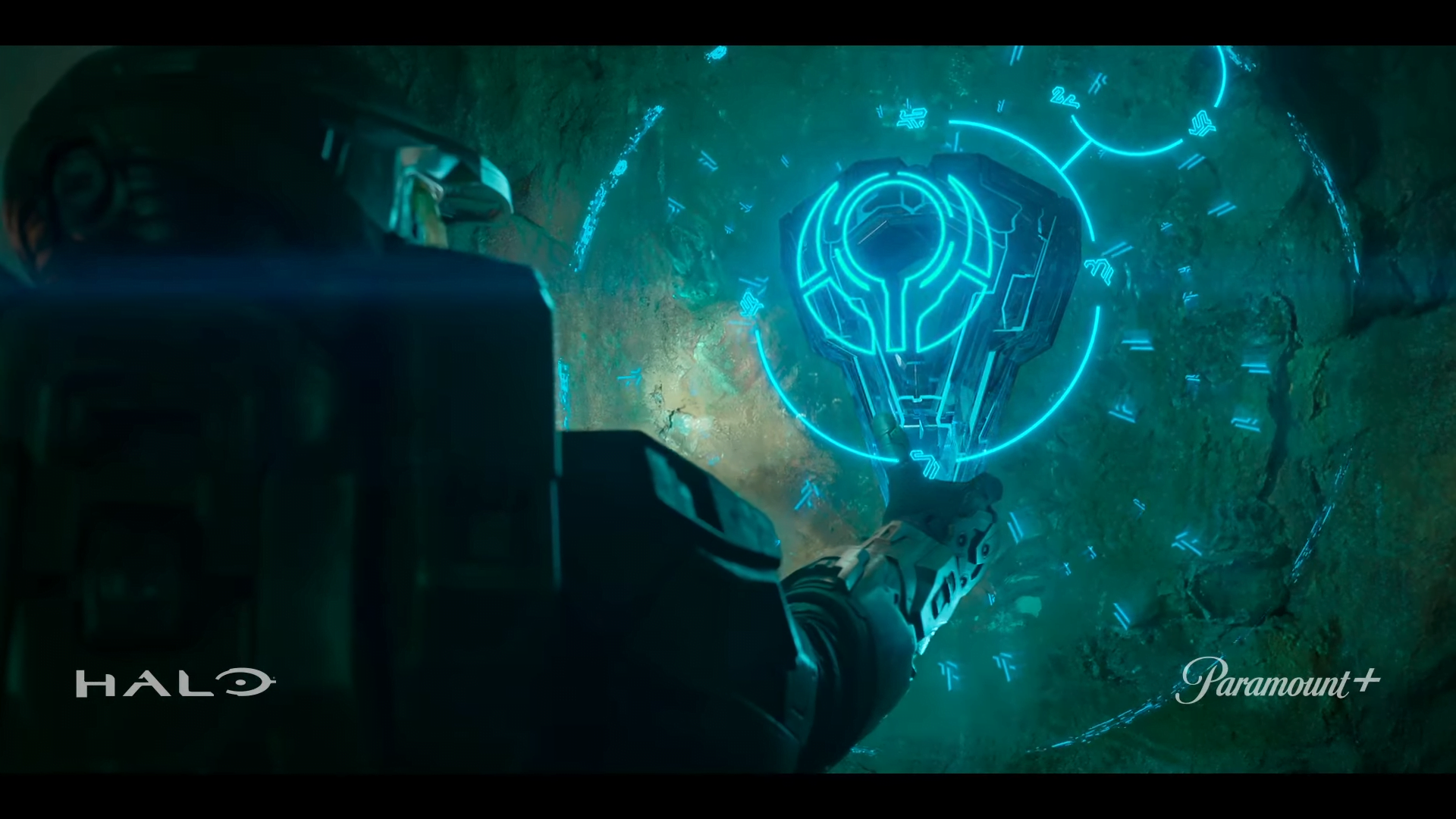 Master Chief touches a Forerunner artifact overlaid by lights and symbols.